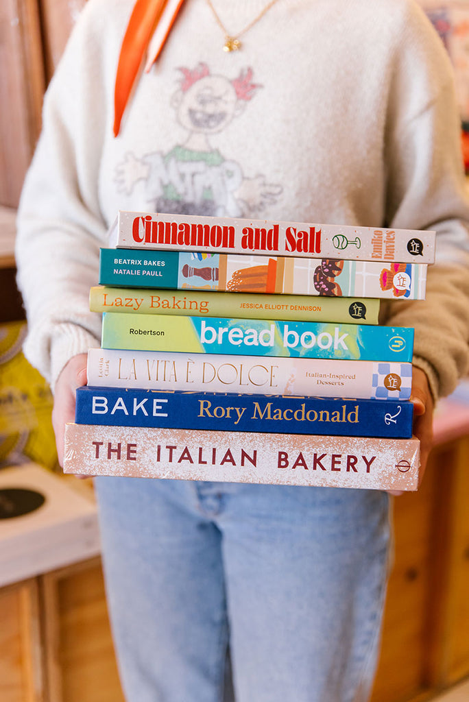 A stack of popular baking cookbooks held in the hands of a staff member at A Quirk of Fate Northcote, photo by Samee Lapham
