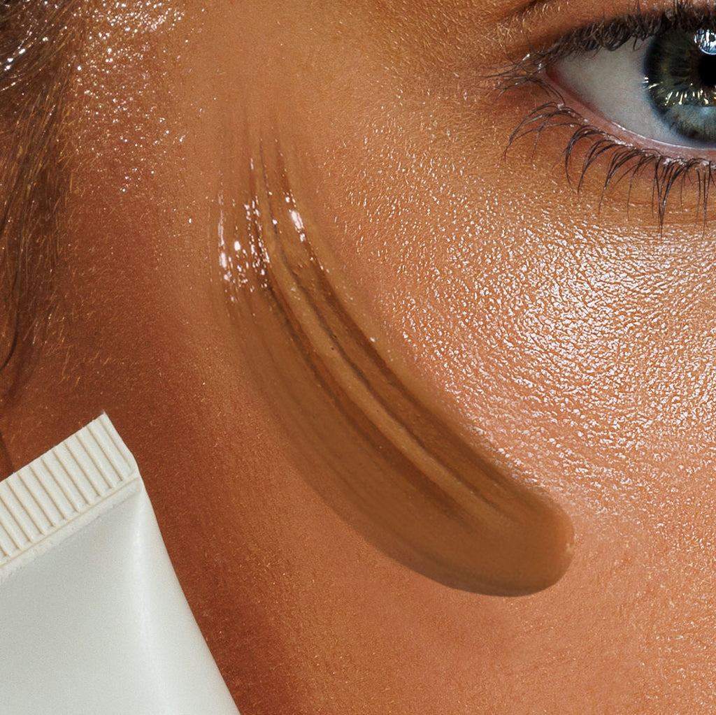 Close-up of a woman's face with a smear of sunscreen on her cheek, next to a tube of sunscreen.